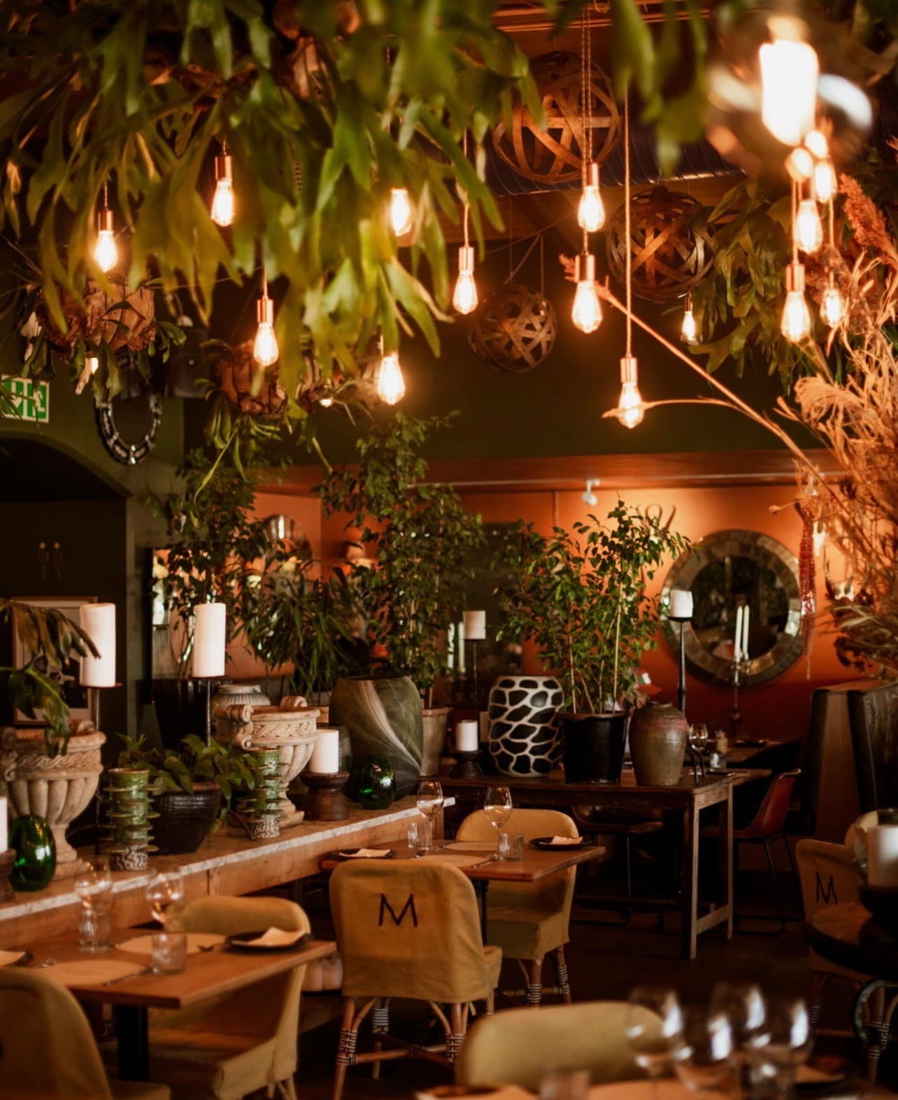The dining room — green foliage ceiling, Edison bulbs and Mantra-monogrammed chairs
