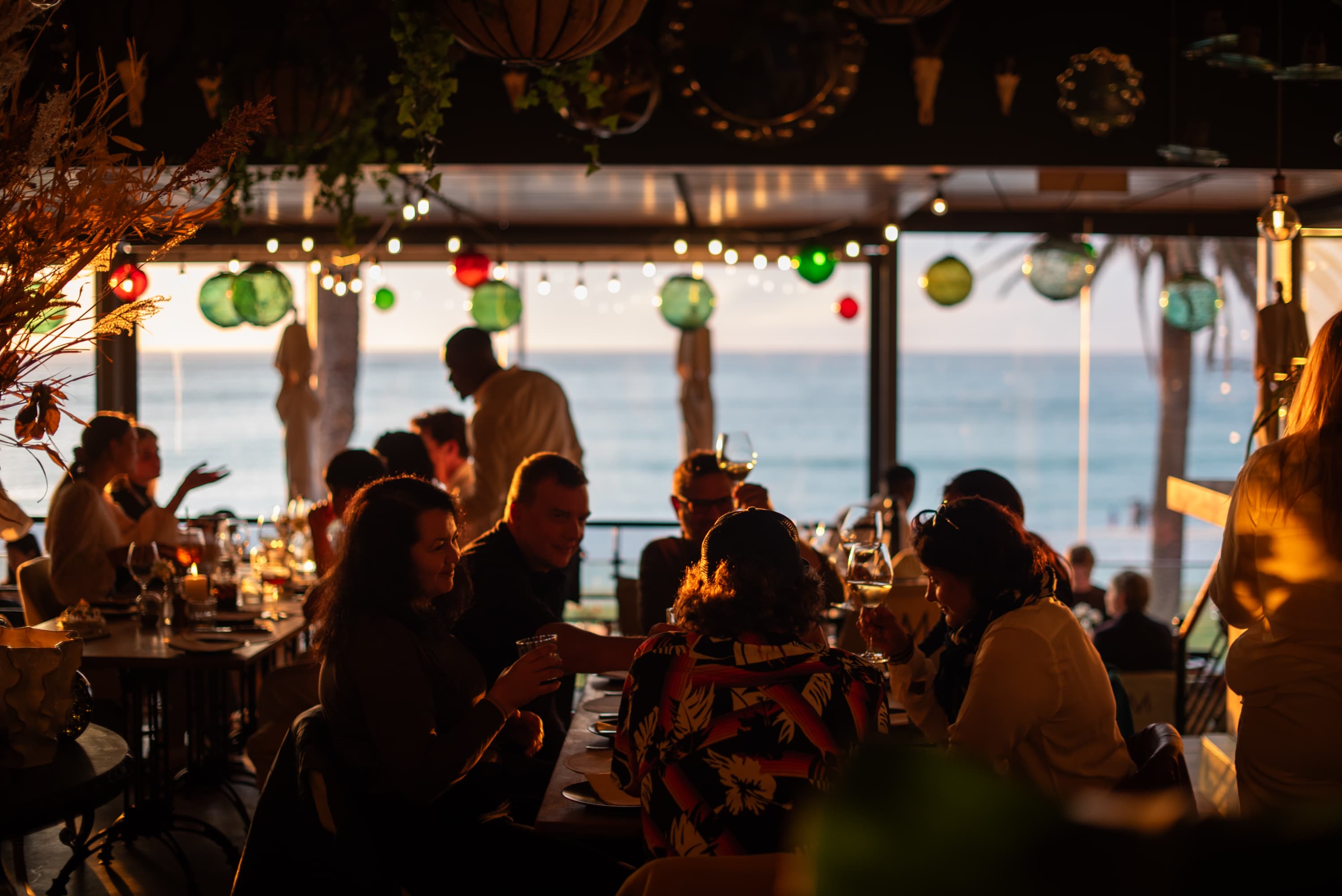 Diners at golden hour under coloured lanterns, the Atlantic stretching to the horizon